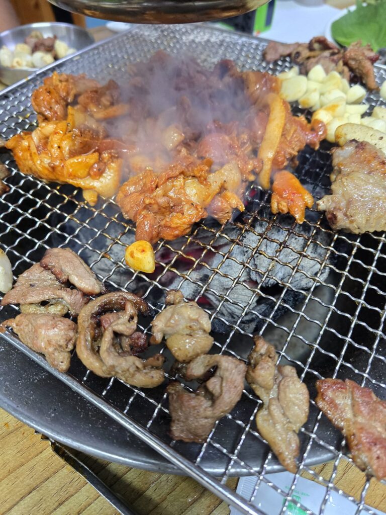 숯불 위 석쇠에서 양념 오리고기와 로스, 마늘을 굽는 모습